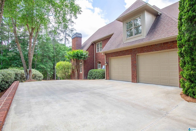 view of home's exterior with concrete driveway, a chimney, brick siding, and a shingled roof