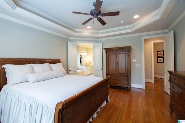 bedroom featuring a raised ceiling, wood finished floors, ornamental molding, a ceiling fan, and ensuite bathroom
