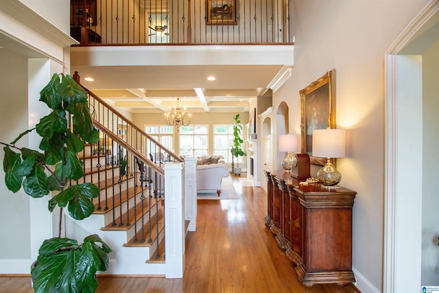 foyer entrance featuring coffered ceiling, a chandelier, stairway, wood finished floors, and baseboards