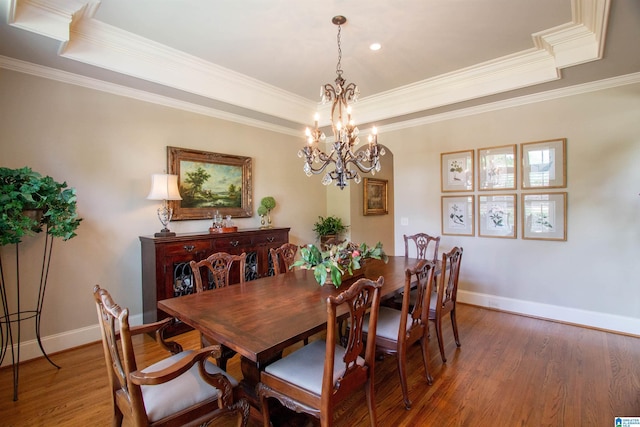 dining area featuring a raised ceiling, ornamental molding, wood finished floors, and a chandelier