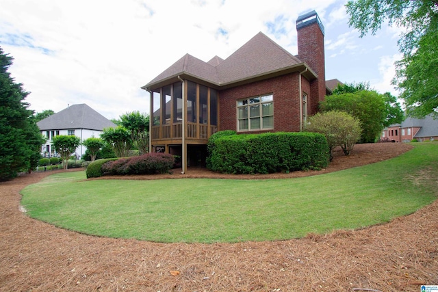 rear view of house featuring a chimney, a sunroom, a yard, and brick siding
