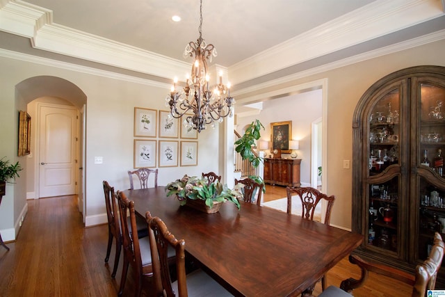 dining area featuring arched walkways, a chandelier, dark wood finished floors, baseboards, and ornamental molding