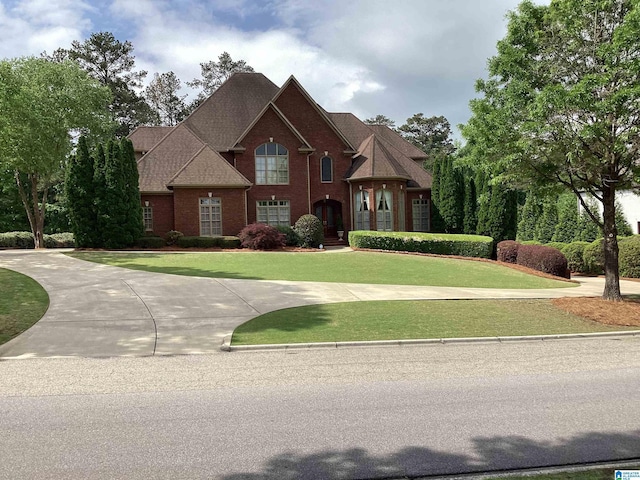 view of front of house with a front yard, brick siding, and curved driveway