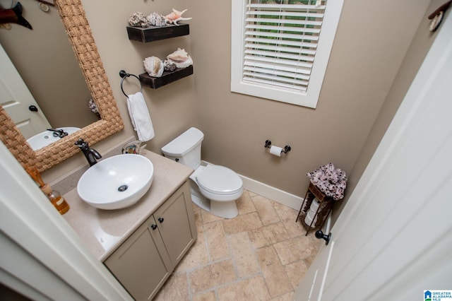bathroom featuring baseboards, vanity, toilet, and stone tile floors