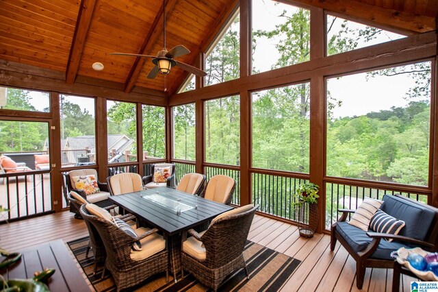 sunroom featuring a forest view, outdoor dining space, ceiling fan, and beamed ceiling