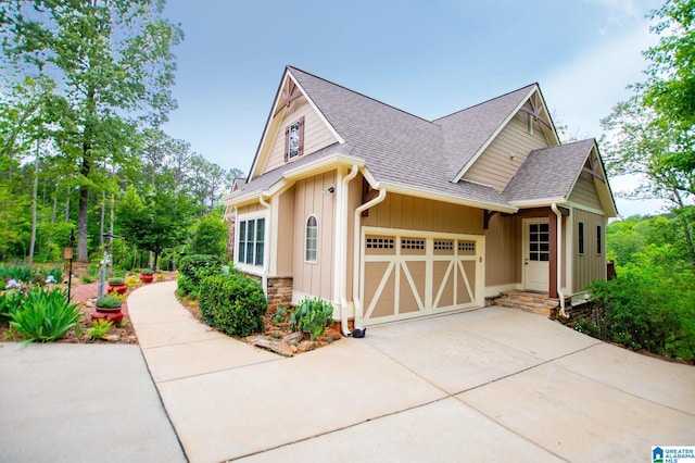 view of side of home featuring stone siding, roof with shingles, board and batten siding, an attached garage, and driveway