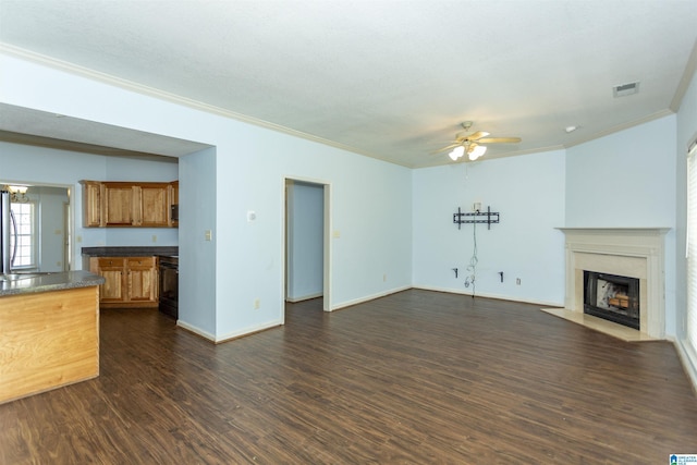 unfurnished living room featuring ornamental molding, dark wood-style floors, visible vents, a ceiling fan, and a fireplace with flush hearth