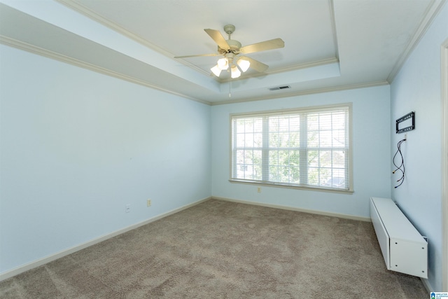 carpeted empty room with visible vents, ceiling fan, a tray ceiling, baseboards, and ornamental molding