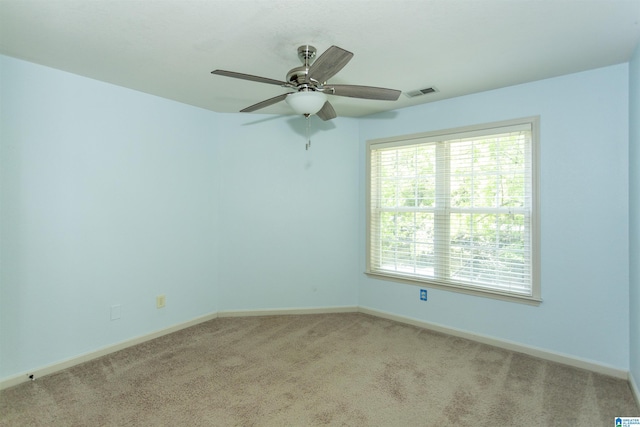 empty room featuring a ceiling fan, visible vents, light colored carpet, and baseboards