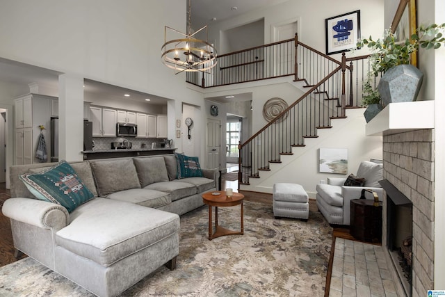 living area with an inviting chandelier, stairway, a fireplace, light wood-type flooring, and a towering ceiling