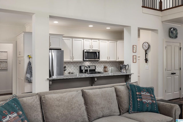 kitchen featuring light stone countertops, stainless steel appliances, ornamental molding, backsplash, and open floor plan