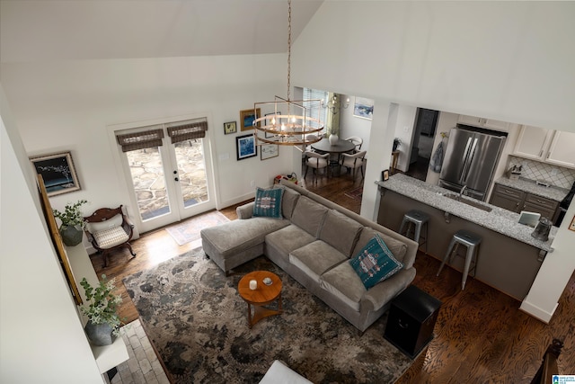 living room featuring high vaulted ceiling, wood finished floors, a notable chandelier, and french doors