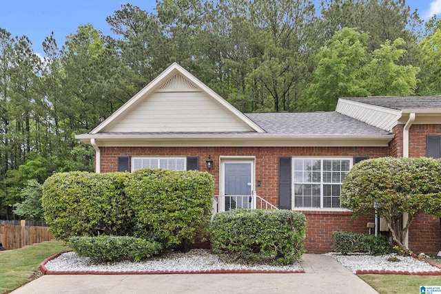 view of front of home with brick siding, fence, and a shingled roof