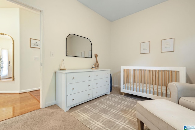 bedroom with a nursery area, baseboards, and light colored carpet