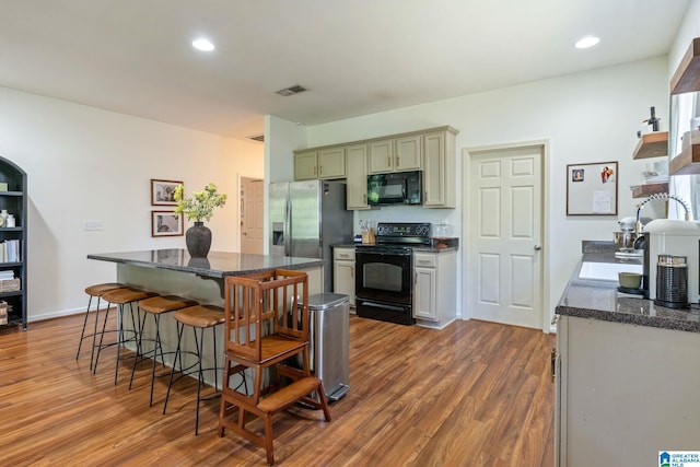 kitchen with wood finished floors, black appliances, a breakfast bar area, visible vents, and a kitchen island