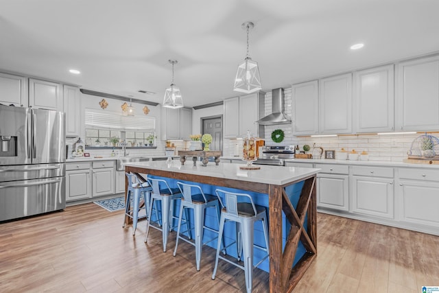 kitchen featuring tasteful backsplash, wall chimney range hood, a breakfast bar, a kitchen island, and appliances with stainless steel finishes