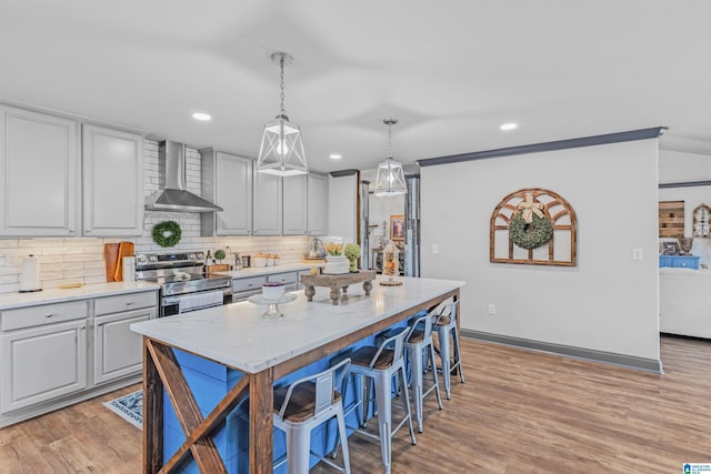 kitchen featuring a kitchen breakfast bar, wall chimney range hood, a kitchen island, decorative backsplash, and stainless steel electric range