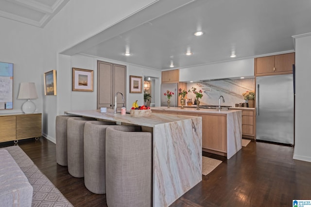 kitchen with built in refrigerator, dark wood-style floors, recessed lighting, and a center island with sink