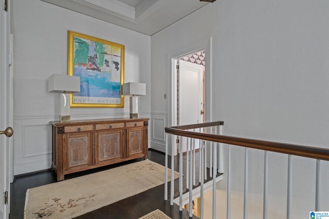 hall featuring crown molding, an upstairs landing, dark wood-style flooring, a decorative wall, and wainscoting