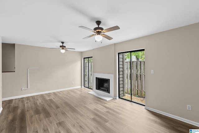 unfurnished living room with a fireplace with raised hearth, a ceiling fan, wood finished floors, and baseboards