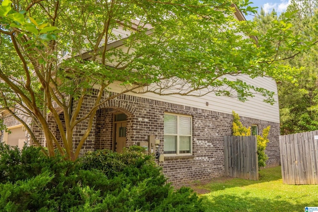 view of property exterior with fence, a yard, and brick siding