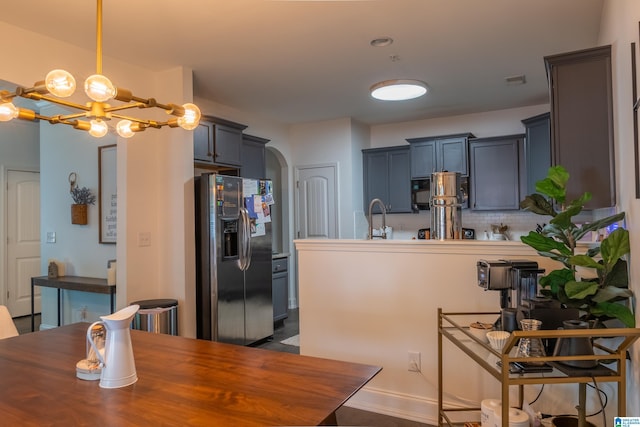 kitchen with decorative backsplash, a sink, arched walkways, a notable chandelier, and stainless steel fridge