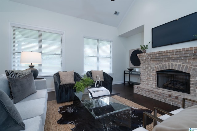 living room with wood finished floors, a brick fireplace, baseboards, visible vents, and lofted ceiling
