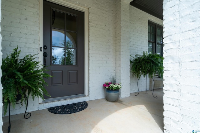 view of exterior entry featuring covered porch and brick siding