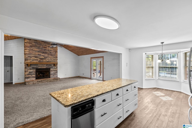 kitchen with vaulted ceiling, a stone fireplace, ceiling fan with notable chandelier, white cabinets, and wood walls