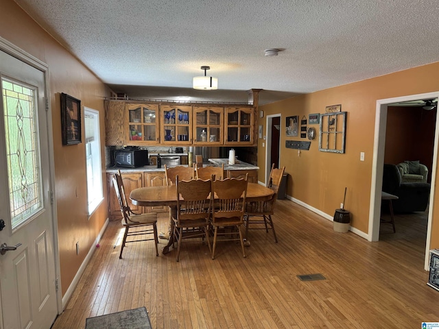 dining space featuring baseboards, a wealth of natural light, a textured ceiling, and light wood-type flooring