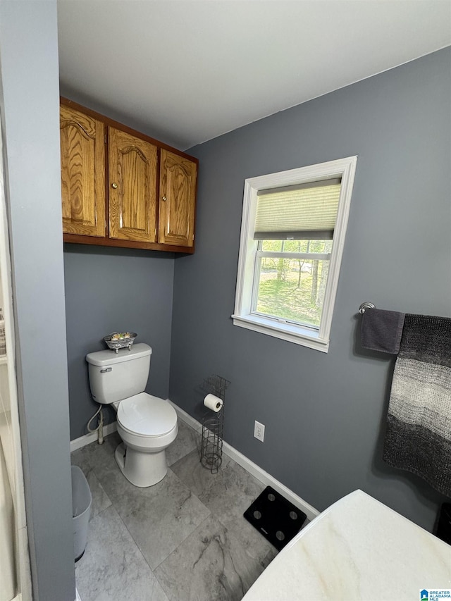 bathroom with marble finish floor, toilet, and baseboards