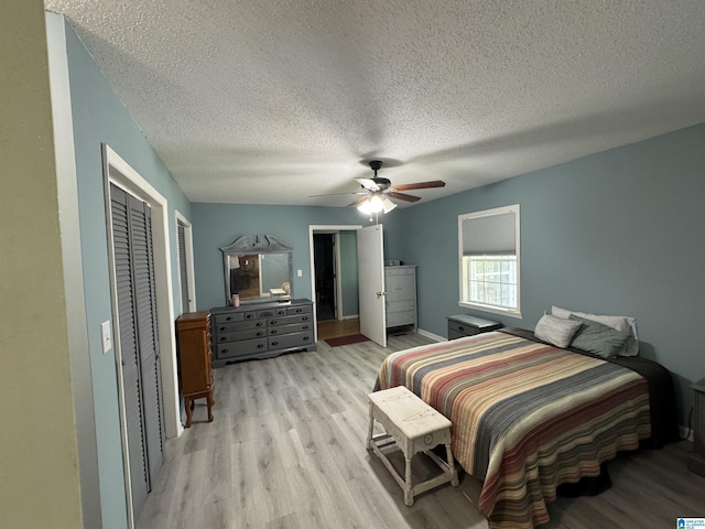 bedroom featuring light wood-type flooring, a textured ceiling, a ceiling fan, and baseboards