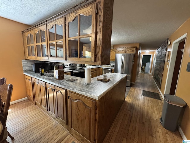 kitchen with stainless steel appliances, a peninsula, a textured ceiling, and dark wood finished floors