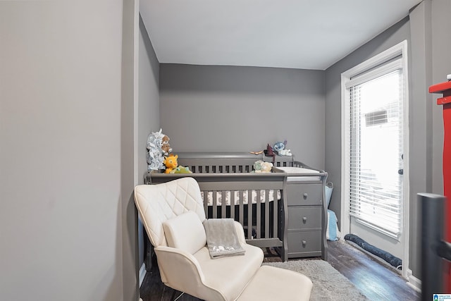 bedroom with a crib, baseboards, and dark wood-style flooring