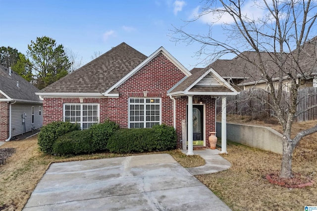 view of front of property featuring fence, brick siding, roof with shingles, and a patio