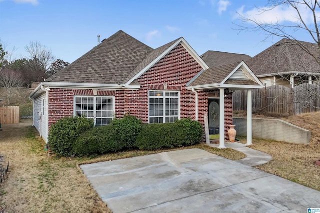 view of front of house with fence, a patio area, roof with shingles, and brick siding