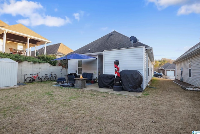 back of property featuring a fire pit, a shingled roof, an outdoor structure, a yard, and a patio