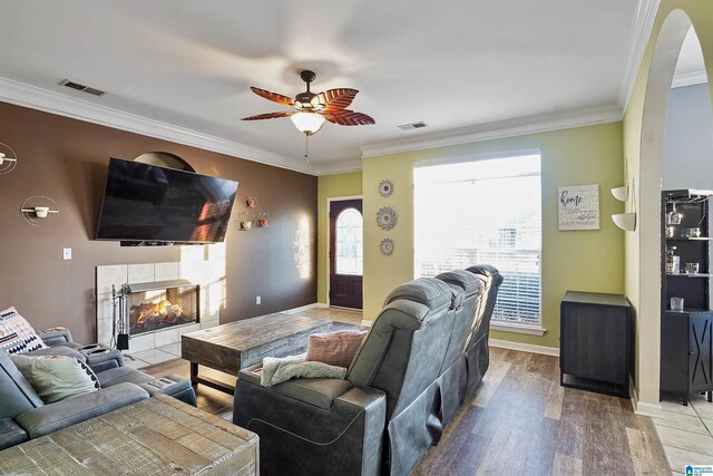 living area with a tiled fireplace, arched walkways, ceiling fan, and crown molding