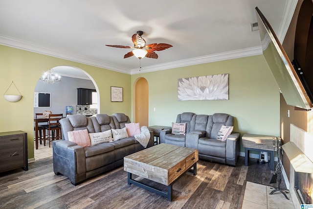 living area featuring arched walkways, wood finished floors, ornamental molding, and ceiling fan with notable chandelier