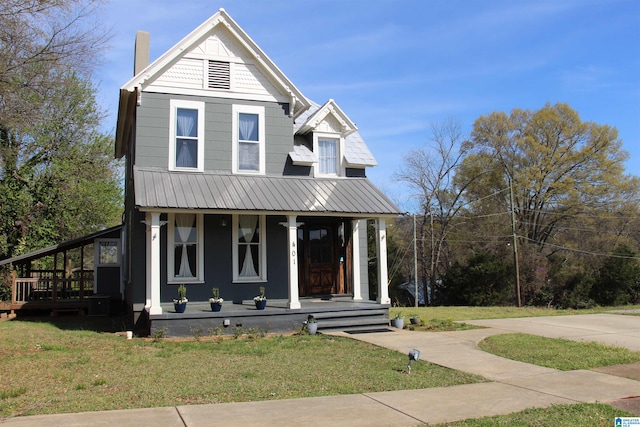 view of front facade with metal roof, a chimney, a front yard, and covered porch