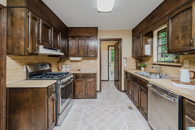 kitchen featuring dark brown cabinets, a sink, appliances with stainless steel finishes, light countertops, and under cabinet range hood