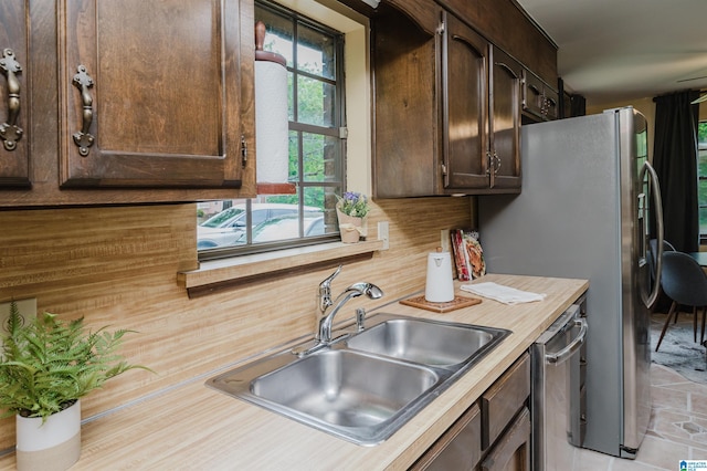 kitchen featuring stainless steel appliances, backsplash, light countertops, a sink, and dark brown cabinetry