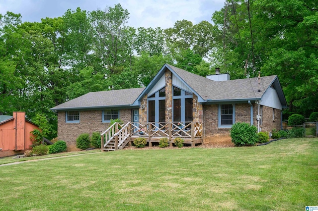 view of front of home featuring roof with shingles, a front lawn, a chimney, brick siding, and a wooden deck