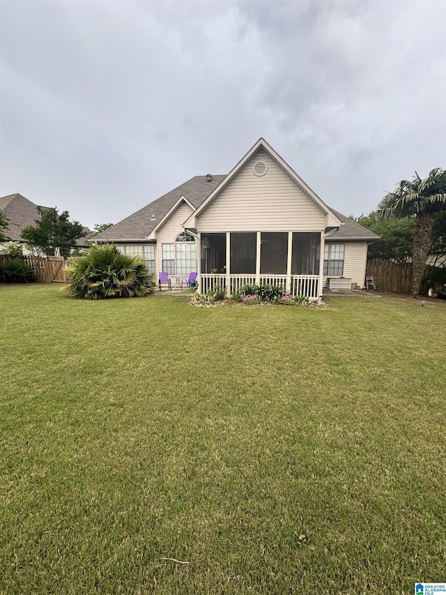 rear view of property featuring roof with shingles, a sunroom, fence, and a lawn