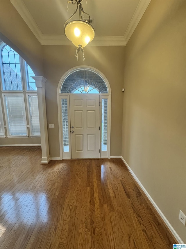 foyer with baseboards, crown molding, wood finished floors, and ornate columns