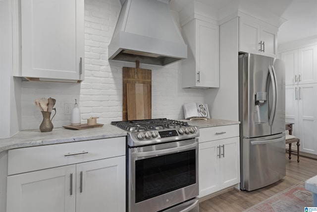 kitchen with backsplash, appliances with stainless steel finishes, light wood-style flooring, custom range hood, and white cabinetry