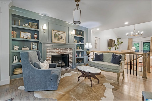 living room with an inviting chandelier, a fireplace, built in shelves, wood finished floors, and lofted ceiling