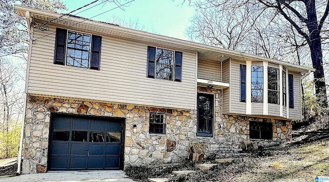 split foyer home featuring an attached garage, stone siding, and driveway