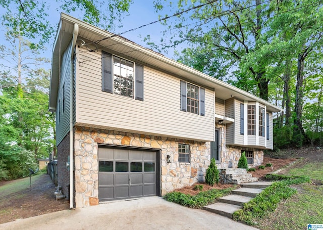 bi-level home with concrete driveway, an attached garage, and stone siding