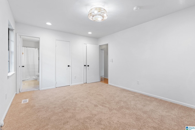 unfurnished bedroom with connected bathroom, visible vents, carpet, baseboards, and multiple closets